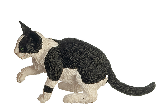A side view of a black and white cat with green eyes, sitting with its right paw raised in a playful pose, on a white background. It has one black spot on its left paw and the rest of its paws and legs are white. Its back and tail are all black. It has a white stripe down its nose, having a typical "mask and mantle" coat pattern.