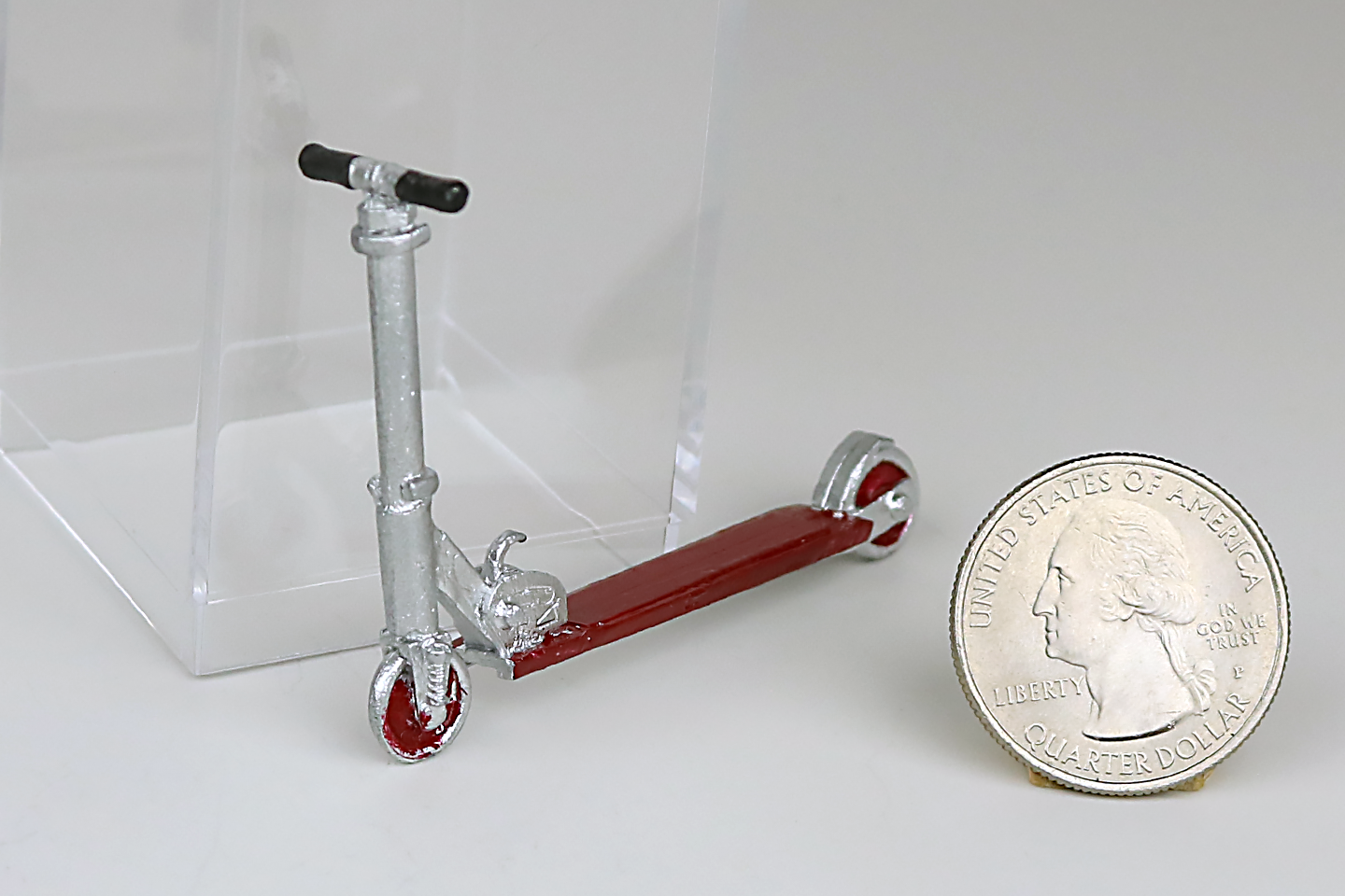 Miniature metal scooter with red accent next to a quarter on a white background