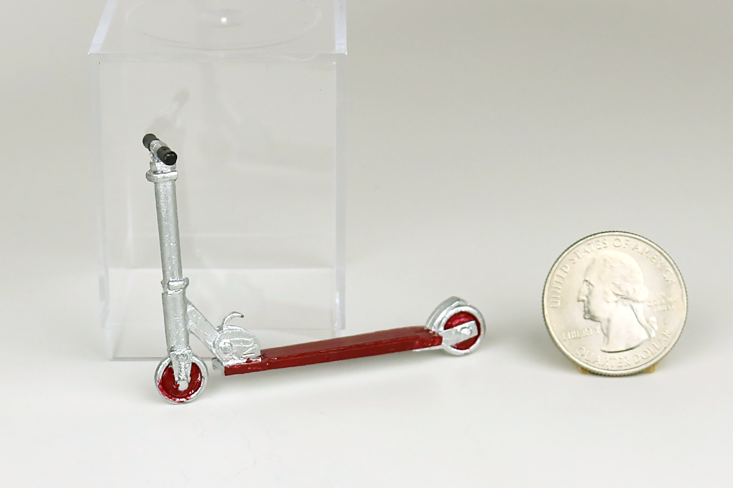 Miniature metal scooter with red accent next to a quarter on a white background