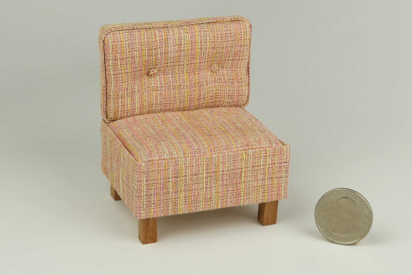 Miniature mid-century modern style side chair with no arms, in a peach-yellow-orange textured fabric, a tufted back with two buttons, and square block walnut legs, next to a quarter for scale on a white background
