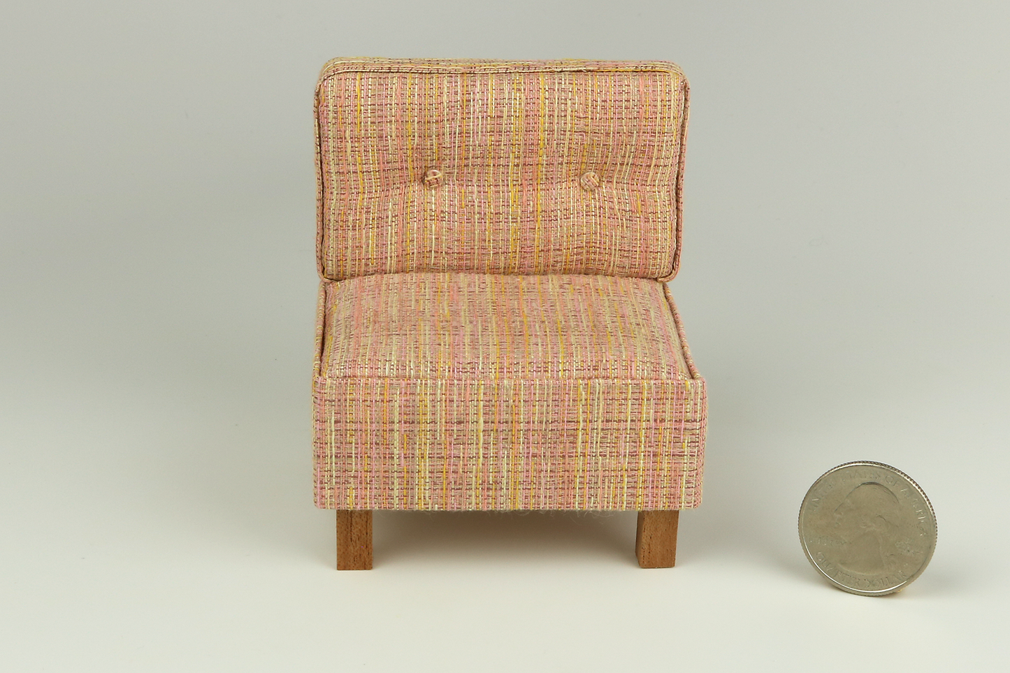 Miniature mid-century modern style side chair with no arms, in a peach-yellow-orange textured fabric, a tufted back with two buttons, and square block walnut legs, next to a quarter for scale on a white background