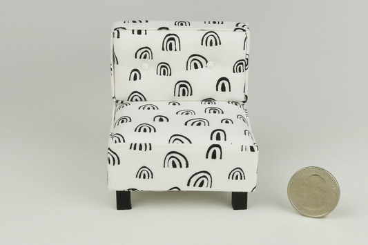 Miniature mid-century modern style side chair with no arms, in a white fabric with black rainbow-shaped patterns throughout, a tufted back with two buttons, and square block walnut legs, next to a quarter for scale on a white background