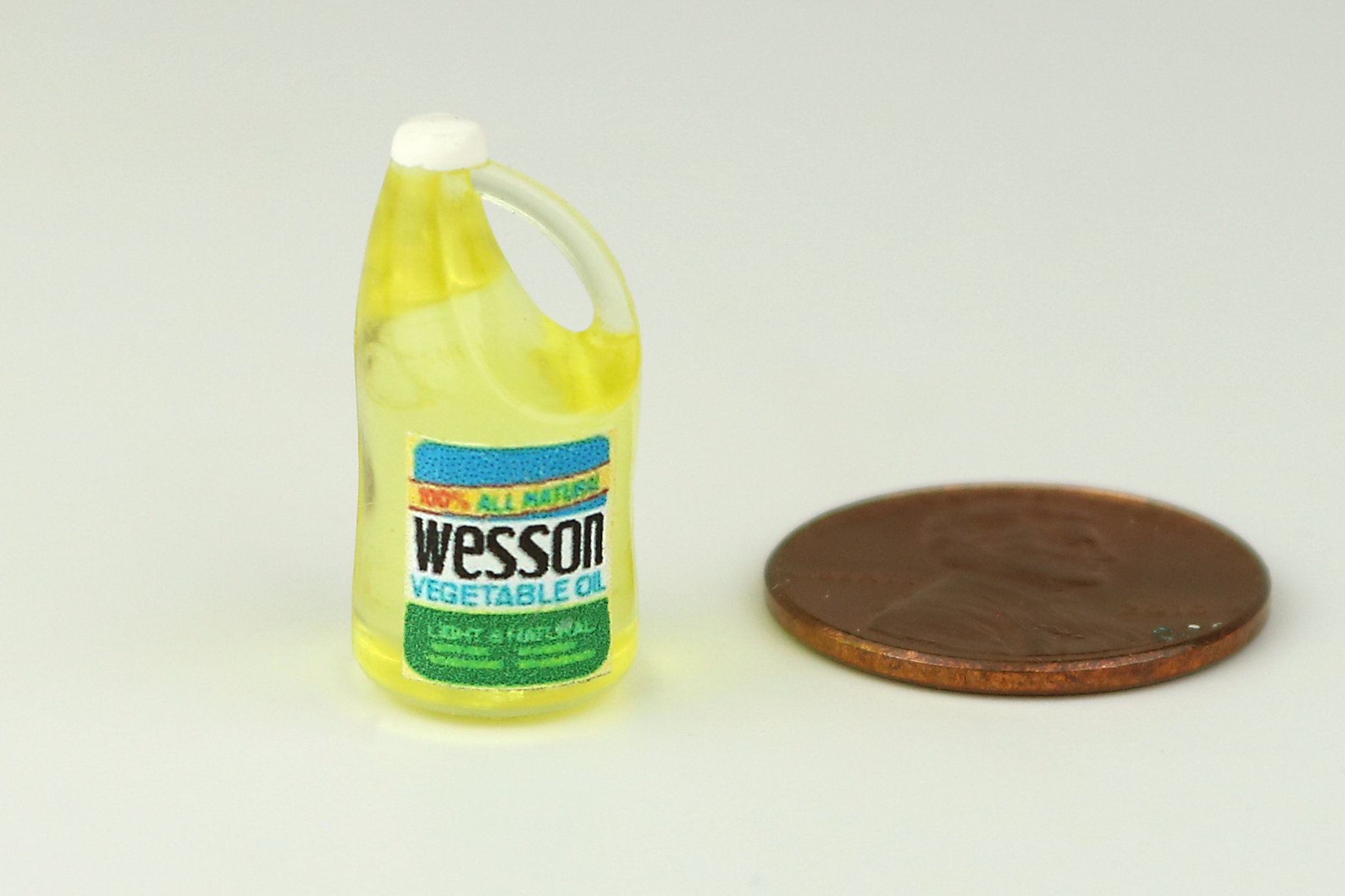 Miniature vegetable oil bottle next to a penny on a white background