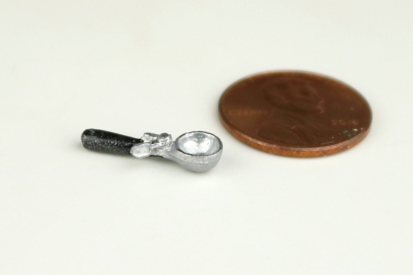 Miniature ice cream scoop with a black handle, next to a penny for scale, on a gray background.