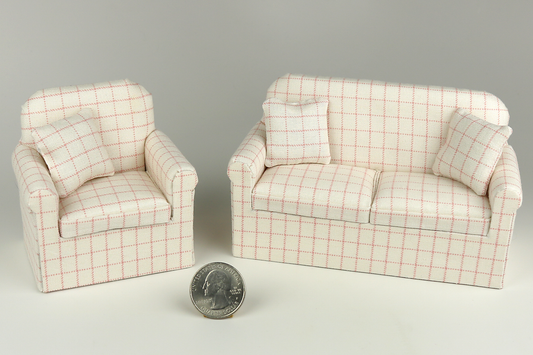Miniature matching armchair and sofa in a pale pink plaid print on a cream background, each with matching pillows, pictured on a gray background, next to a quarter for scale.