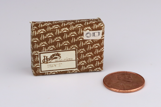 Small brown packaging box with a "Houseworks" brand logo next to a penny for scale on a light gray background