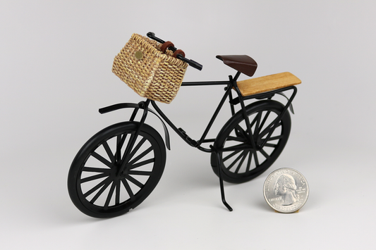 Miniature black bicycle with a basket next to a quarter for scale on a light gray background.
