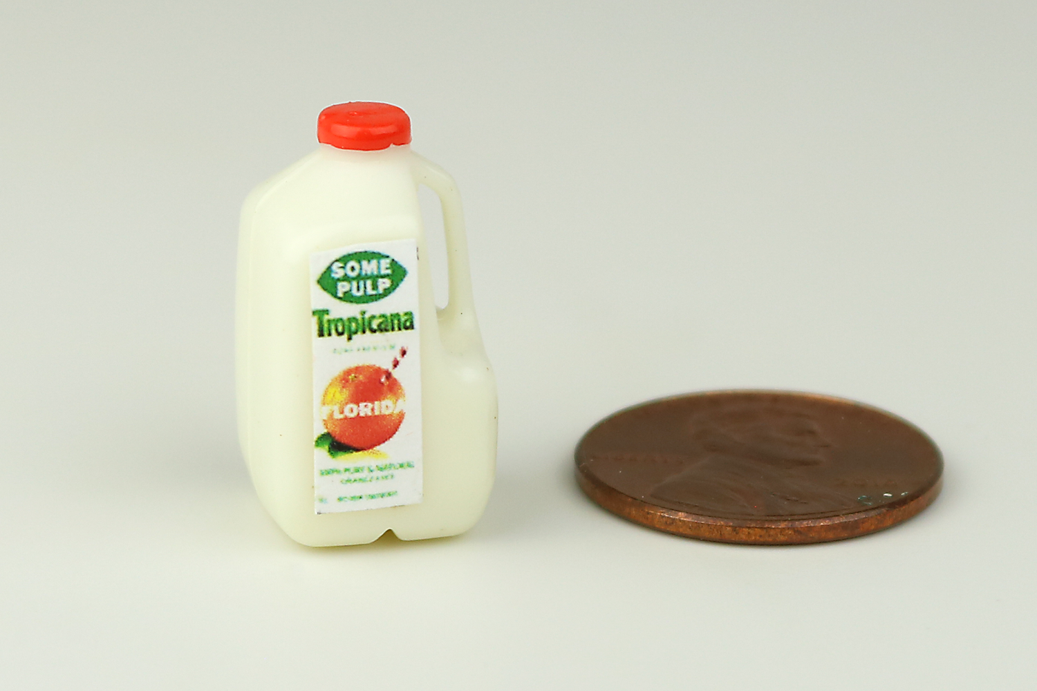 Miniature orange juice jug next to a penny on a white background