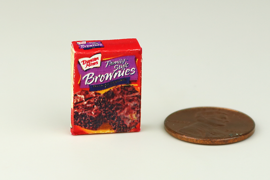 Miniature box of brownie mix next to a penny on a white background