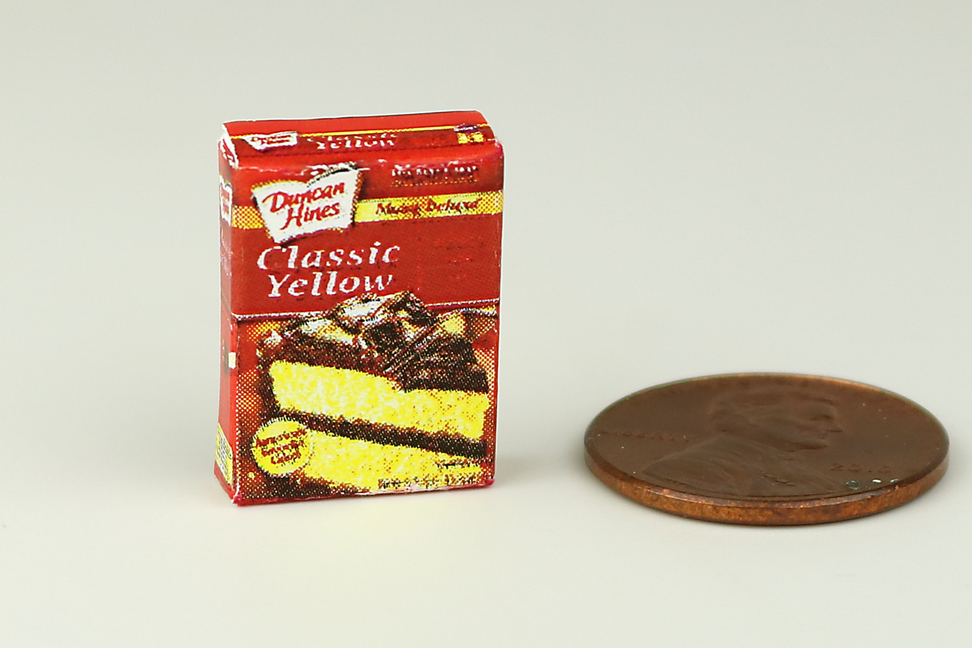 Miniature box of yellow cake mix next to a penny on a white background