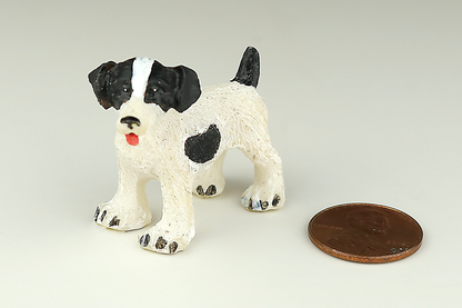 Jack Russell Terrier miniature dog figurine with black and white spots next to a penny on a light gray background