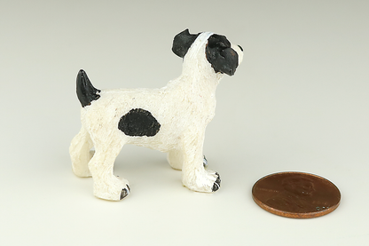 Jack Russell Terrier miniature dog figurine with black and white spots next to a penny on a light gray background