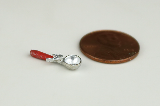 Miniature ice cream scoop with a red handle, next to a penny for scale, on a gray background.