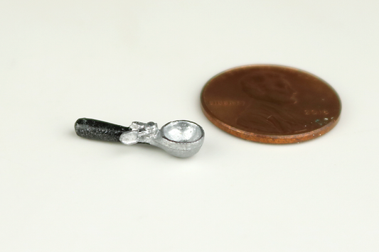 Miniature ice cream scoop with a black handle, next to a penny for scale, on a gray background.