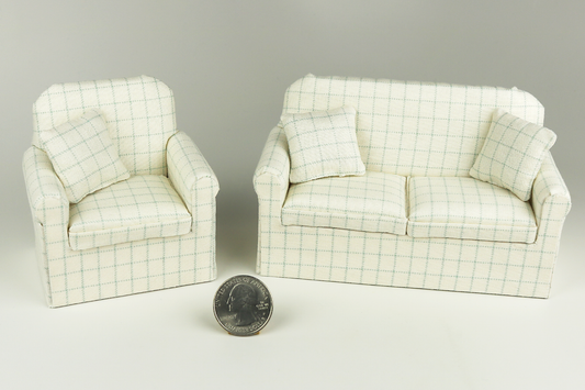 Miniature armchair in a pale robin's egg blue plaid print on a cream background, next to a matching sofa in the same pattern, each with matching pillows, pictured on a gray background, next to a quarter for scale.