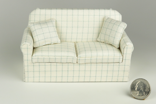 Miniature sofa in a pale robin's egg blue plaid print on a cream background, with a matching pillow, pictured on a gray background, next to a quarter for scale.