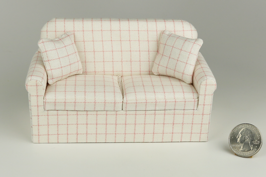 Miniature sofa in a pale pink plaid print on a cream background, with matching pillows, pictured on a gray background, next to a quarter for scale.