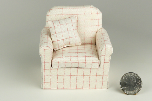 Miniature armchair in a pale pink plaid print on a cream background, with a matching pillow, pictured on a gray background, next to a quarter for scale.